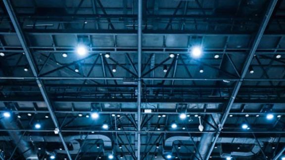 A ceiling in an industrial building, lined with pipes, beams and lights