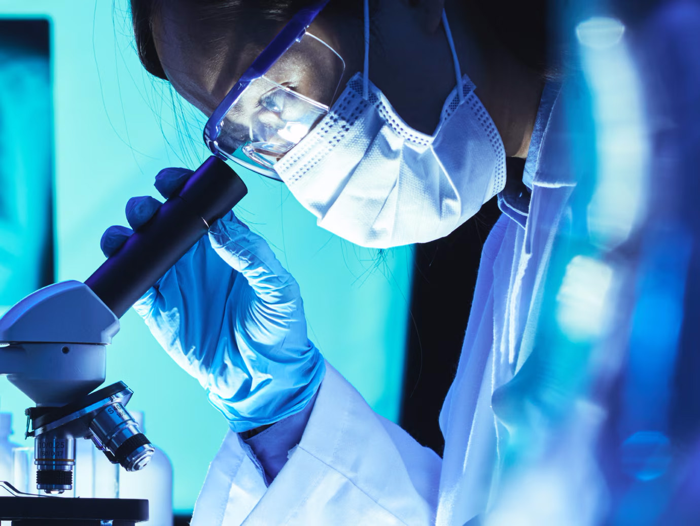 Profile view of a scientist in lab gear examining a microscope
