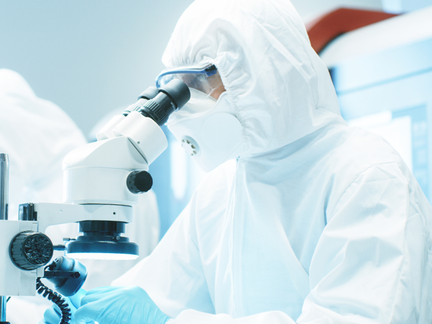 A scientist wearing a protective suit and looking into a microscope