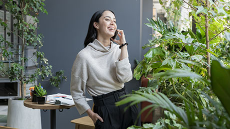 Woman smiling while having a conversation on her phone, surrounded by indoor plants in room