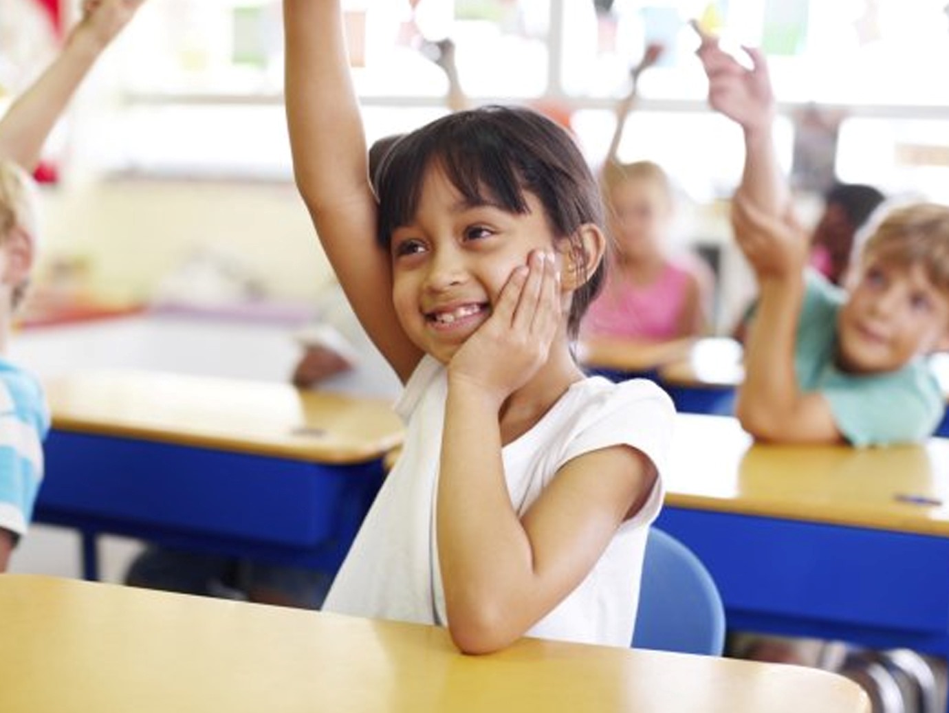 Group of children raising their hands in the classroom