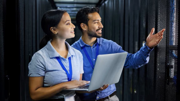 Two engineers-observing a data server rack while one holds a laptop in her handspagelist