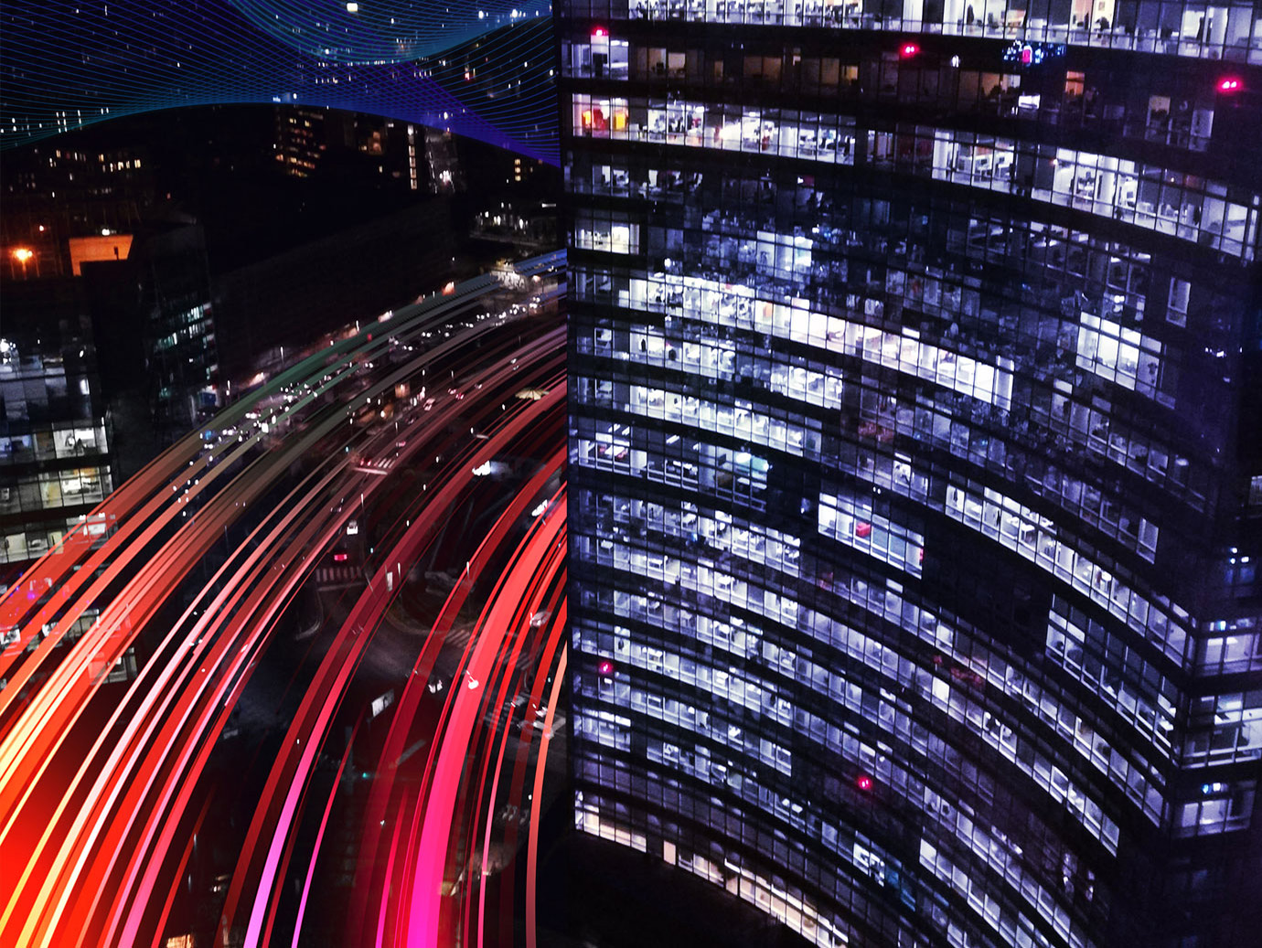 Aerial view of a skyscraper lit up at night along a busy highway 