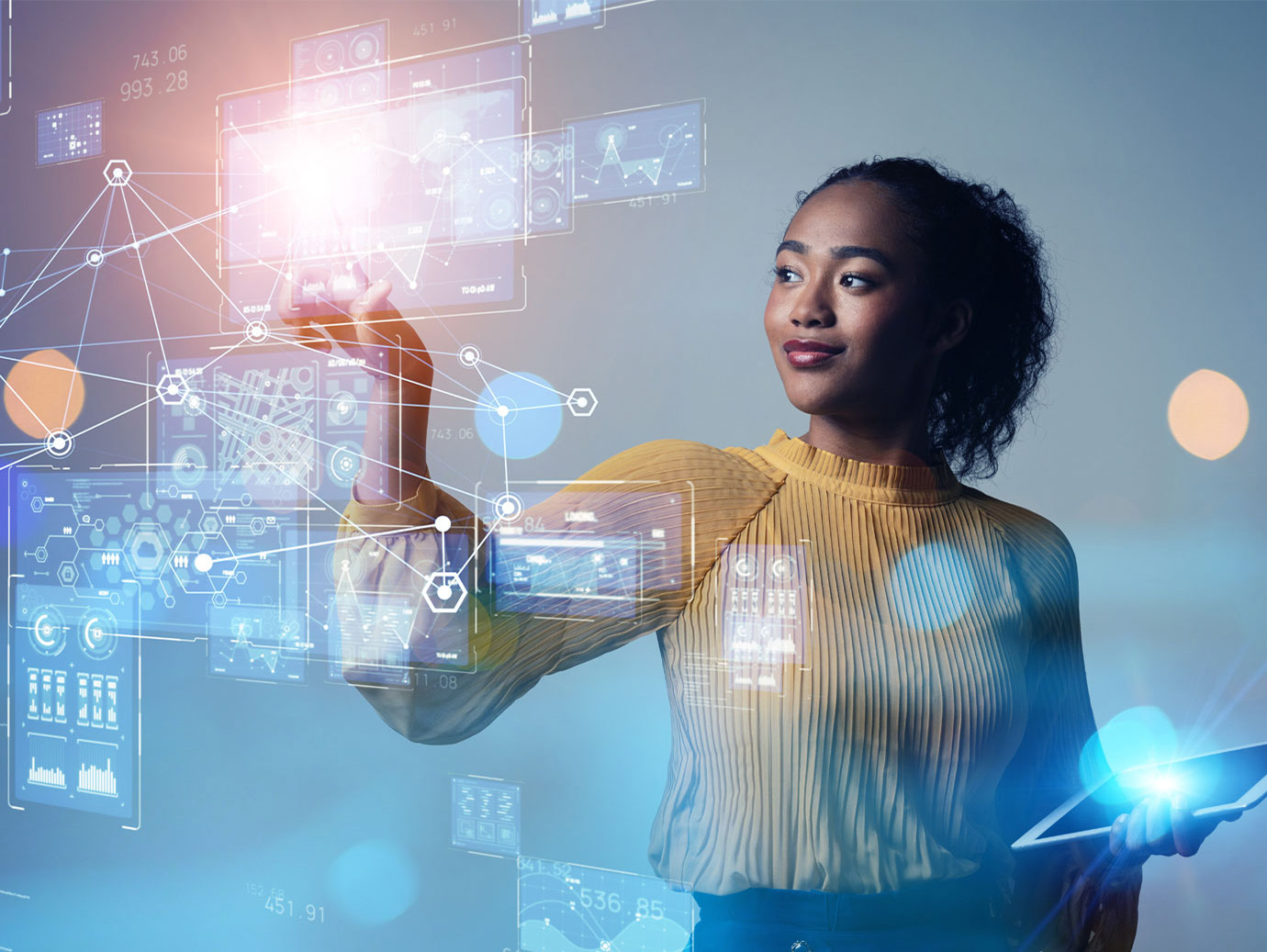 A woman holding a tablet while smiling and pointing at holographs showing line graphs
