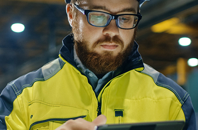 A person wearing a hard hat and glasses looking at a tablet