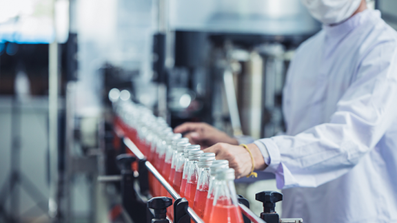 Bottles with a red liquid going through a conveyor belt in a manufacturing unit