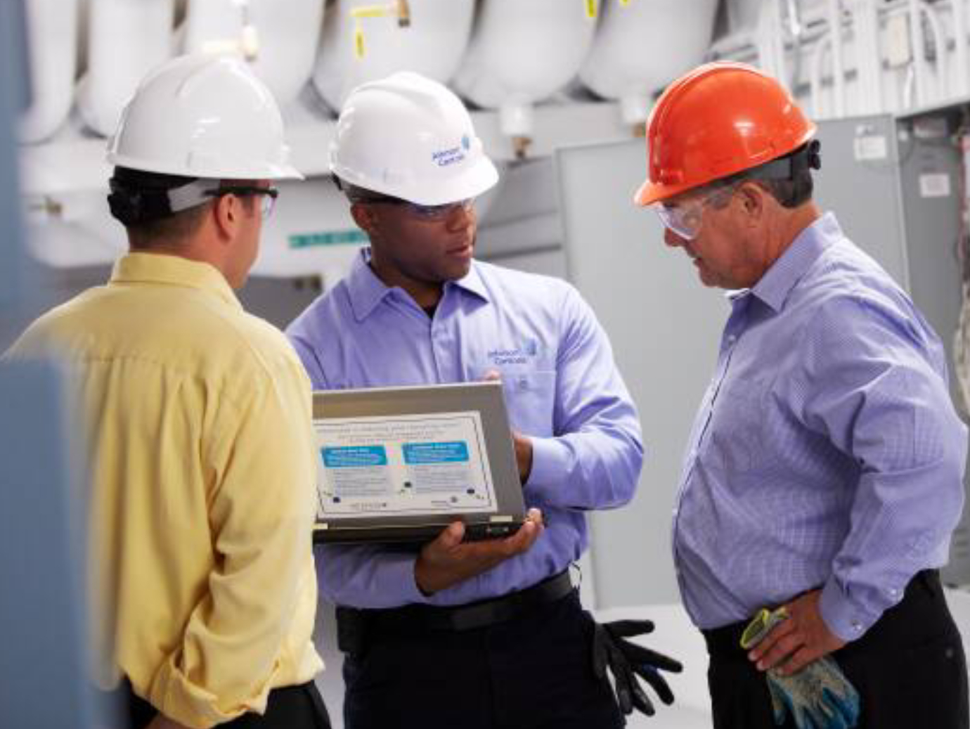 Three maintenance engineers discussing, while one of them holds a laptop