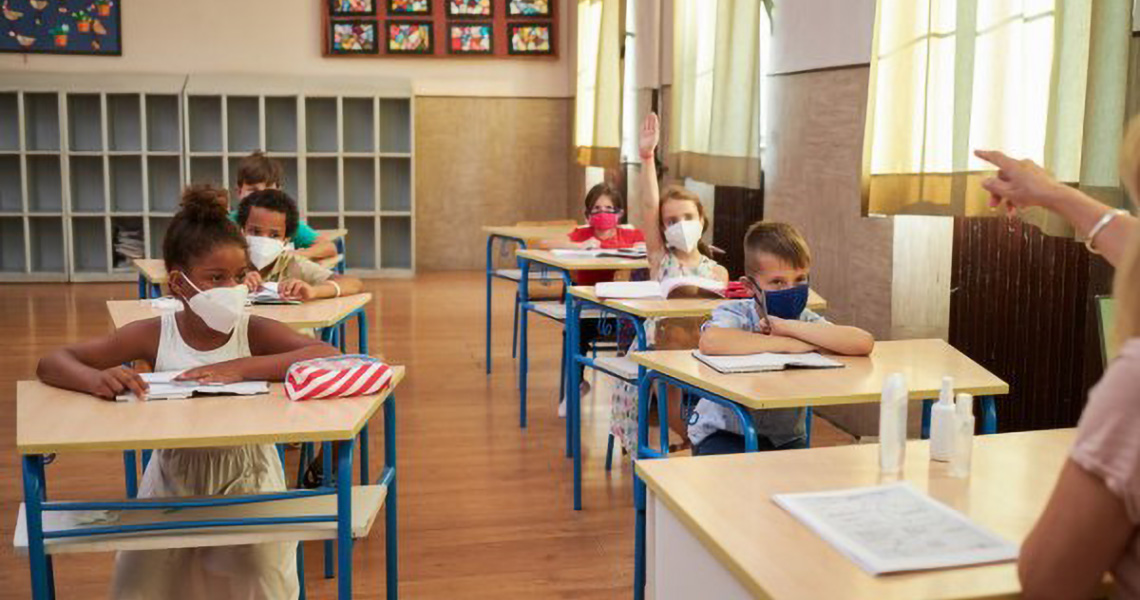 Elementary students in a classroom, with one student with their hand raised