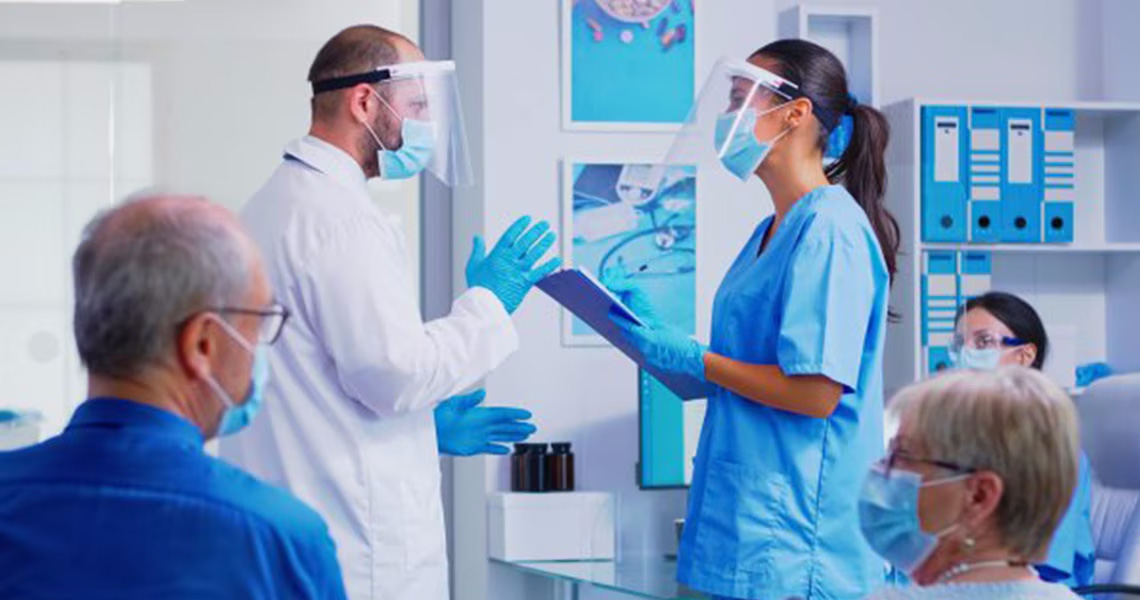 Two medical staff talking in a consultation room with patients sitting