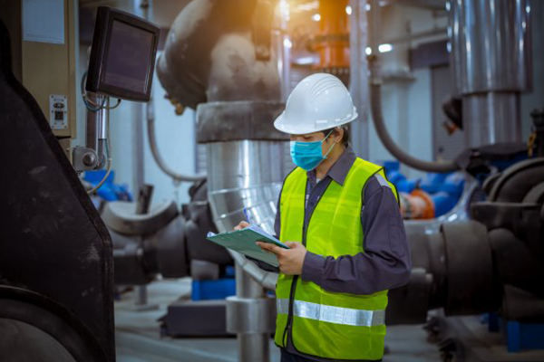 An engineer in protective gear reading a tablet in an industrial facility