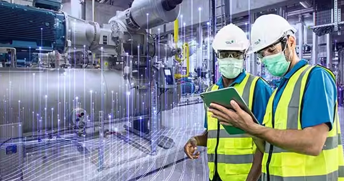 Two maintenance workers wearing facemasks and looking at a screen-tablet, in an industrial space"