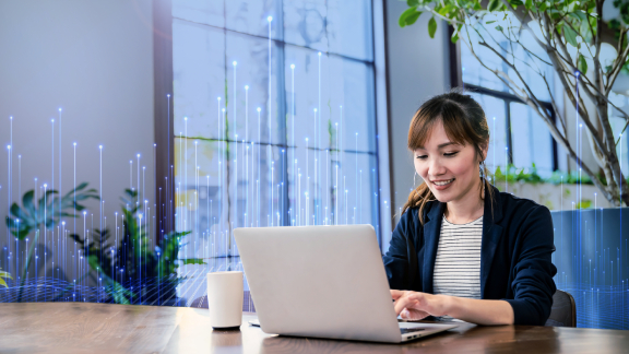 Female employee working on her laptop in office, overlaid with a graphic of transmission nodes in the backgroound