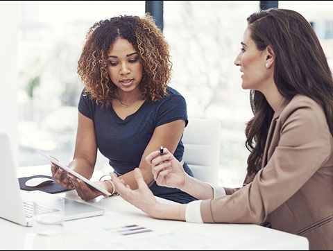 Two female colleagues discussing work over a laptop and a tablet