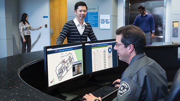 Security officer working on a computer at the front desk, as a customer watches