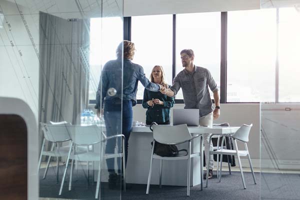 Man and woman smiling and shaking hands with a female client in a conference room