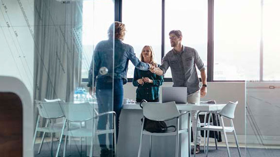 Man and woman smiling and shaking hands with a female client in a conference room