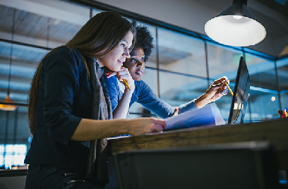 Two women working in front of a laptop with pencils in their hands