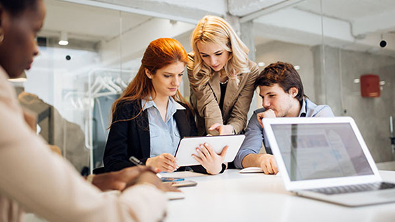 Three employees in discussion at a table, with one holding a tablet