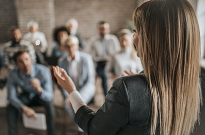 Back view of a woman speaking with people sitting in the background