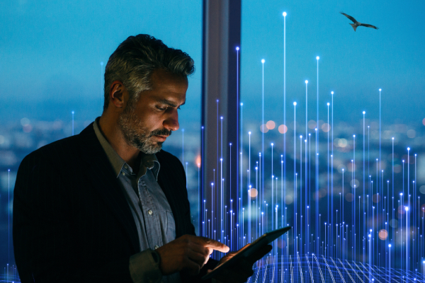 A man standing by a window and scrolling on a tablet, with OpenBlue graphics in the background