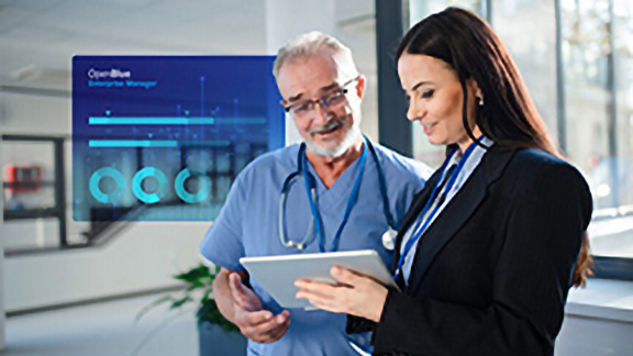 A doctor and a businesswoman reading a writing pad, with a blue OpenBlue poster overlaid in the background