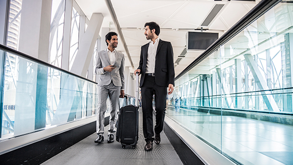 Two men carrying luggage and talking in an airport