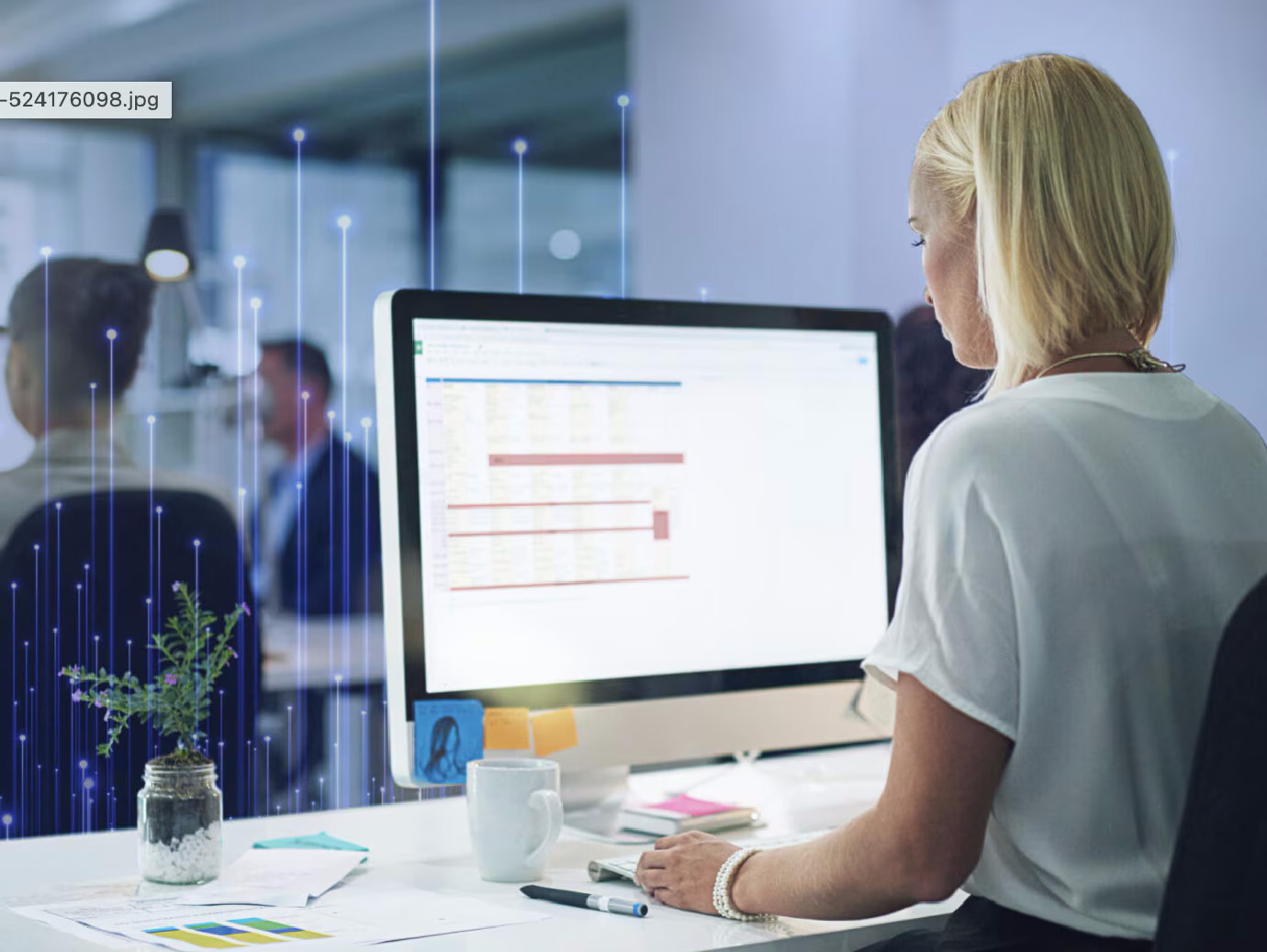 A woman working on a PC in her cubicle, with other colleagues working in the background