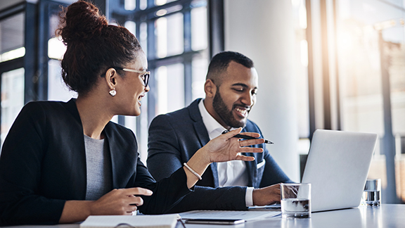 A woman in an office pointing at the laptop of the man seated beside her