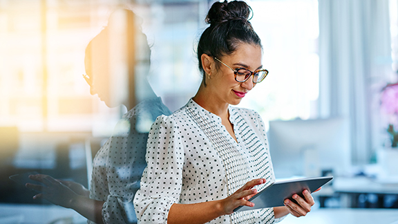 A woman wearing glasses scrolling on a tablet and smiling