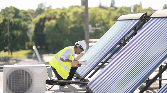 A female engineer writing on a clipboard near a set of solar panels