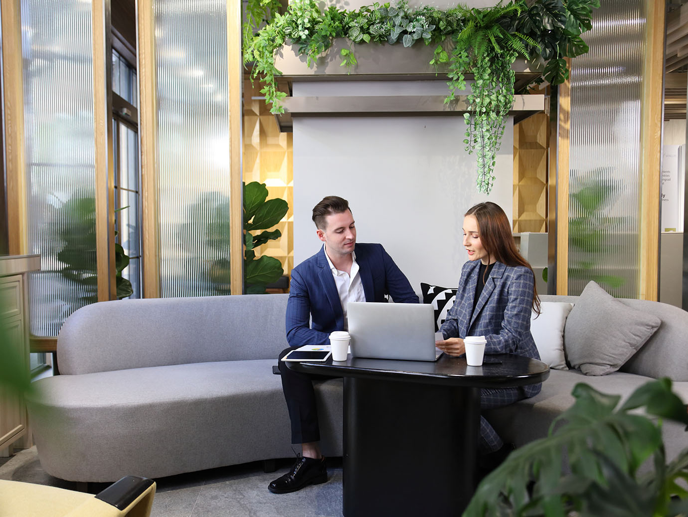 A man and woman sitting on a sofa and looking at a laptop in an office building