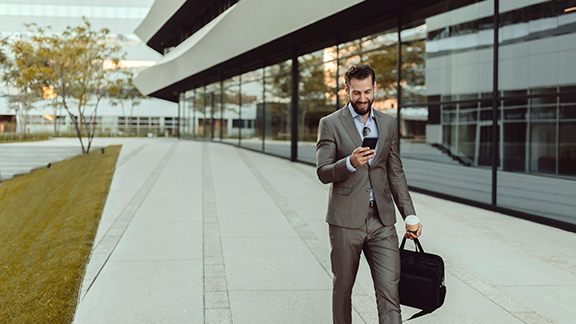 A man looking at his phone and walking along a corporate building