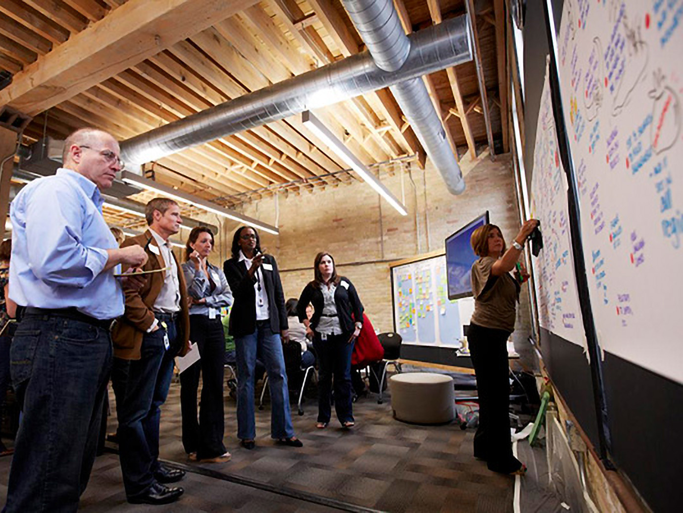 People standing watching a woman writing on a board on a wall